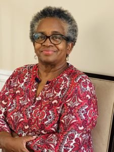 Photo of African American woman with short hair wearing glasses and a red shirt sitting down