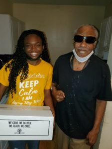Young black woman holding a meal box standing next to an older black man wearing sunglasses